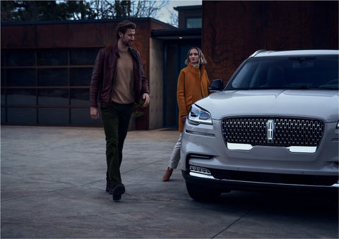 A man and a woman approaching a 2023 Lincoln Aviator® SUV, which illuminates certain lights when they are close | Brinson Lincoln of Athens in Athens TX